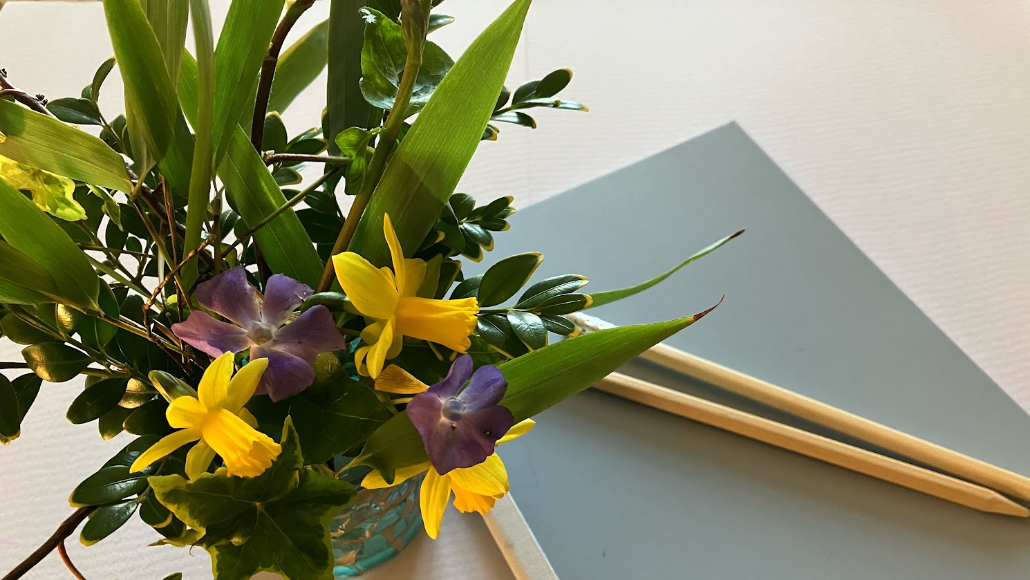 Spring flowers in a small vase, with a closed notebook and a pencil.